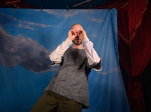 Gilbert makes a binocular shape with his hands, looking through to the camera.